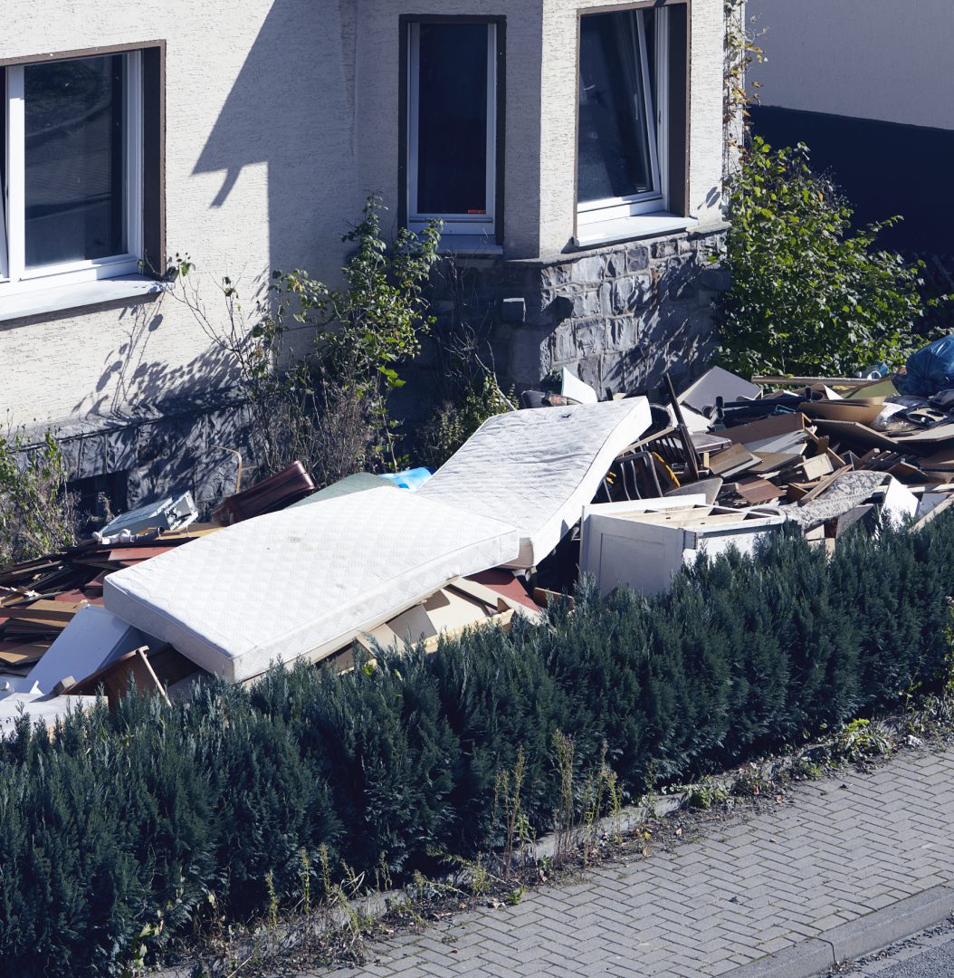 Discarded furniture outside building near hedge.